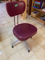 Front and side view showing red pleather seat and backrest, chrome frame, and caster wheels on floor tile.