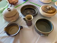 Photo showing six pottery pieces including three lidded bowls, one mug, and two small serving bowls with different glazes.