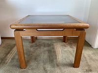 Front view of wooden side table with glass top showing wood texture and rounded edges.