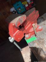 Side angle view of Craftsman red bench vise mounted on wooden workbench, showing tightening handle and mounting screws.