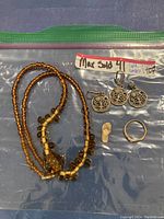 Full lot showing all jewelry items inside plastic bag including amber necklace, silver earrings, pendant, gold ring and charm