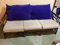 Front view of bamboo couch showing three beige seat cushions and two large blue velvet back cushions.