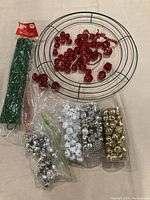 Photo showing metal wreath frame, bundles of green pipe cleaners, red jingle bells both loose and clustered.