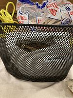 Close-up of black metal mesh basket with various kit contents inside, including wrapped yellow rope and bags of wooden clothes pegs.