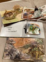 Photo showing open pages of some pop-up books, including detailed 3D pop-up dinosaur scenes.