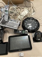 Photo showing various electronic items including cordless phone with base, wall clock, Lenovo tablet, remote, and cords.