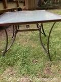 Outdoor square table on grass showing metal frame and glass top with paint marks.