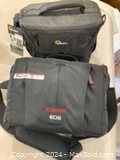 Front view of two black camera bags, one Canon EOS and one Lowepro with tags attached