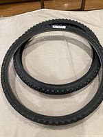 Two black bicycle tires displayed on cloth surface, showing knobby tread and overall tire shape.