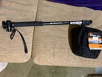Vanguard monopod fully extended showing foam grip and wrist strap on beige surface