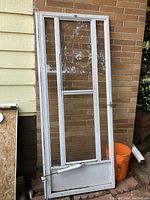 Full view of the aluminum frame screen door leaning against a wall, showing the missing mesh and sliding glass panel.