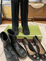 Three pairs of women's size 9.5 footwear including tall black Roots boots, black leather ankle boots, and embroidered Seychelles high heels.
