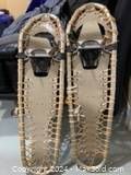 Front view of the pair of traditional wooden snowshoes with woven webbing and strap bindings, showing overall condition and string repairs.