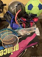 Photo showing various sports equipment including tennis rackets, roller blades, gloves, and a large black exercise ball.