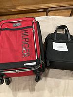 Full view of two suitcases side by side on a white cloth, one large red Tommy Hilfiger suitcase and one smaller black suitcase.