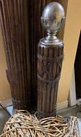 Close-up of large wooden tiki bar pillar with intricate carved design and unscrewable polished metal topper, next to wooden hanging curtain.