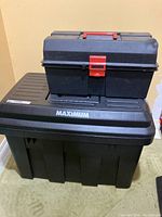 Stacked large and smaller Maximum brand black plastic tool chests. Larger chest on bottom labeled Maximum, smaller chest on top with red latch and handle.