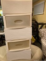 Photo of two stacked Umbra storage units with drawers visible. Units are white with oval cutout handles, positioned on a wheelchair in a basement or garage room.