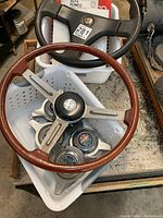 Overhead view of wood-rim and black vinyl steering wheels, manuals, and knock-off spinners in a tote