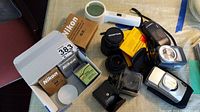 Photo showing multiple items including Nikon filter boxes, Sixtron light meter, Vivitar and Soligar lenses, and others on table surface.