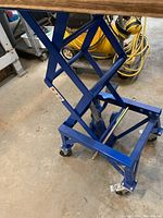 Side view of blue steel hydraulic dirt bike lift showing the scissor mechanism and caster wheels
