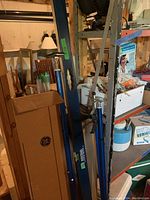 View of the basement shelving area showing blue levels with handles and a box of GE fluorescent bulbs nearby along with metal spacer bars