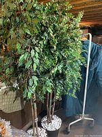 Two large faux trees each in a black pot with white stones, showing full foliage and multiple trunks.