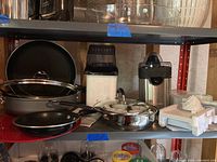 Overview of cooking pans, Cuisinart juicer, mandoline slicer, egg poacher, and popcorn popper on shelves in basement storage area.