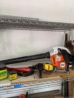 Full view of Stihl BG 56 C leaf blower on metal shelf with rigid intake tube and shoulder strap.
