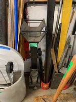 View of the manual log splitter vertical beam with wedge and hydraulic jack base, placed against a wall next to other garden tools.