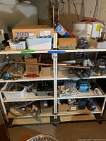 Shelving unit showing a variety of plumbing parts including plastic piping, metal fittings, connectors, hardware and electrical cords, all stored neatly