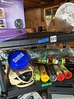 Shelf with Holmes Lil Blizzard fan box, two small oscillating fans, several cans of tennis balls including Dunlop and Wilson brands, a green lawn bowling ball bag with balls, and a blue Konica film canister.