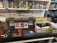 Closed gray Handyman tool box and surrounding hardware boxes on shelf and bench