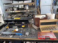 Wide view of the assortment of hand tools including wrenches, sockets, screwdrivers, and hardware laid out on a table.