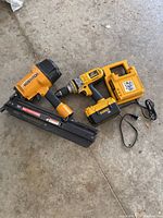 DeWalt cordless drill, charger, and Bostitch power nailer on concrete floor.