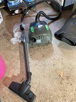 Green and gray Bissell Velocity canister vacuum cleaner with hose, metal extension wand, and floor nozzle on concrete floor.