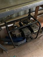 Side view of gasoline-powered water pump in protective black metal frame with blue hose coiled beside it.