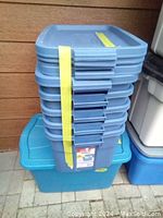Stack of five Rubbermaid Roughneck storage totes with matching lids. The totes are blue-gray color and appear sturdy and durable.