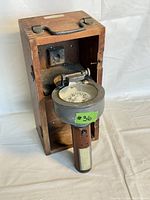 Antique hand compass partially out of its wooden carrying box, showing handle and main compass body.