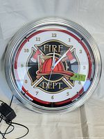 Front view of Fire Department wall clock, showing clock face with emblem, numbers, and chrome frame with neon strip off.