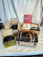 Four cardboard boxes filled with vintage 45 RPM records and a red Rhythm Tote carrier sitting atop the boxes.