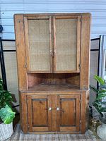 Front view showing entire corner hutch with woven cane panel doors upper cabinet and solid wood panel doors lower cabinet.