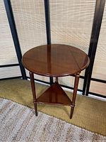 Photo of Bombay drop leaf table with one leaf extended showing round wooden top and triangular shelf lower portion.