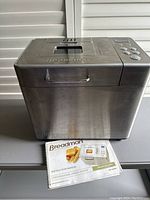 Breadman stainless steel breadmaker with control panel and instruction manual in front.