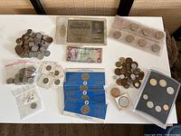 Top-down overview of all coins and currency laid out on white surface showing bags of coins, coin holders, banknotes, and commemorative coin packs.