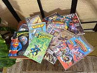 Photo showing front cover comics such as Superman, Vext, The Adventures of Superman, Deadman, Azrael, Hawkman, The Centurions, and others arranged on a wooden chair.