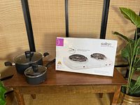 Cooktop and pots displayed alongside the original box on wooden table with plant visible in background.