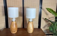 Two wooden base table lamps with white cylindrical shades on a wooden table.