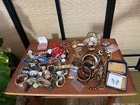Wide shot of entire jewelry lot on wooden table showing watches, bracelets, necklaces, earrings, rings and small decorative basket with floral designs.