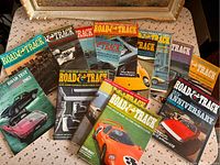 14 Road & Track magazines laid out on a table showing various classic car magazine covers from the 1970s including an anniversary edition.